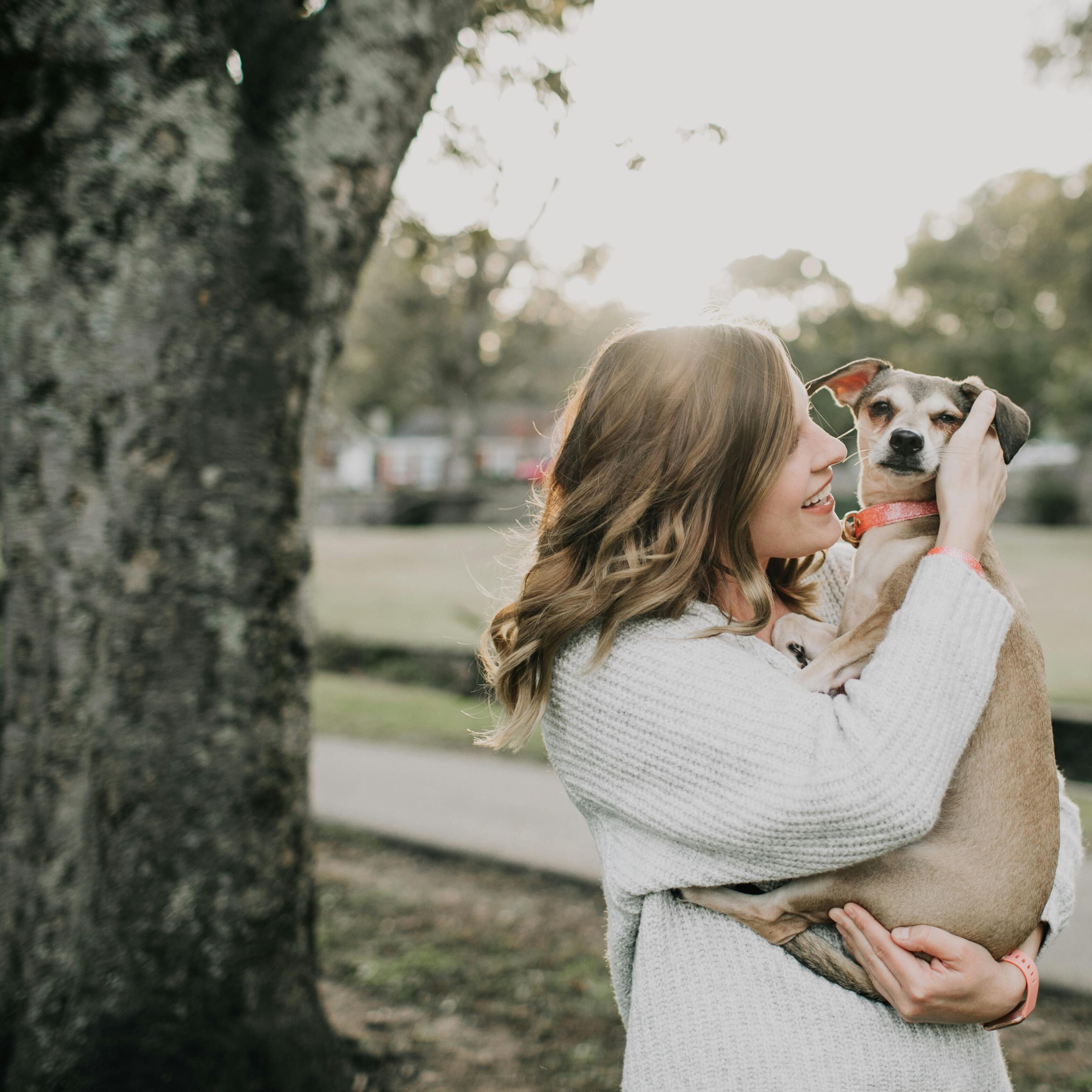 woman holding her small dog in a park in summer