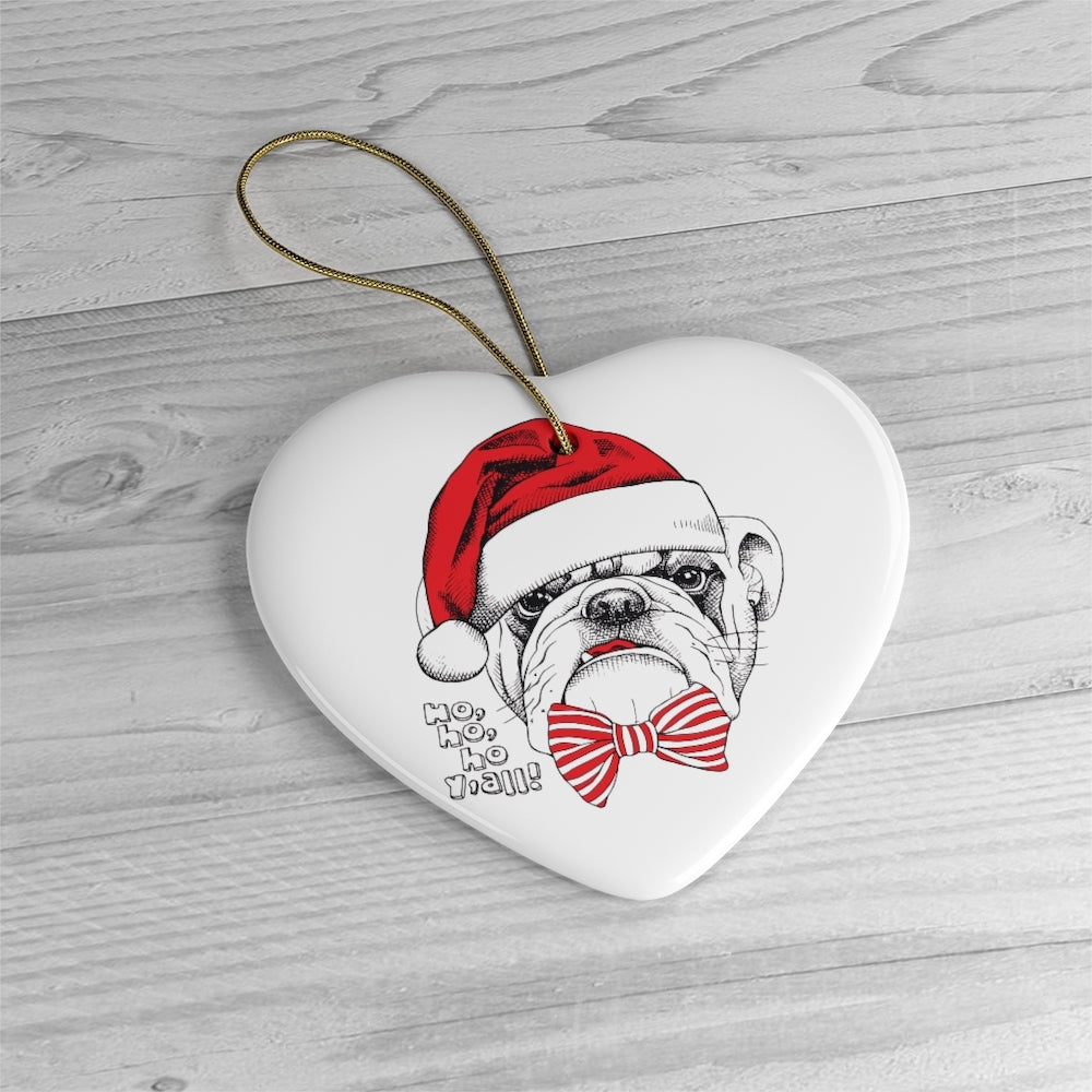 Heart-shaped Christmas ornament with a bulldog wearing a Santa hat and bow tie on a wooden surface.