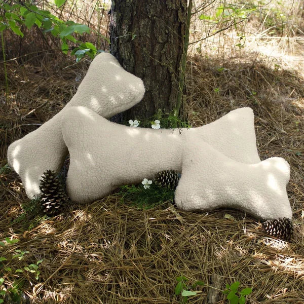 Three bone-shaped pillows on the ground next to a tree in a natural setting