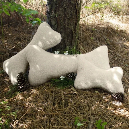 Three bone-shaped pillows on the ground next to a tree in a natural setting