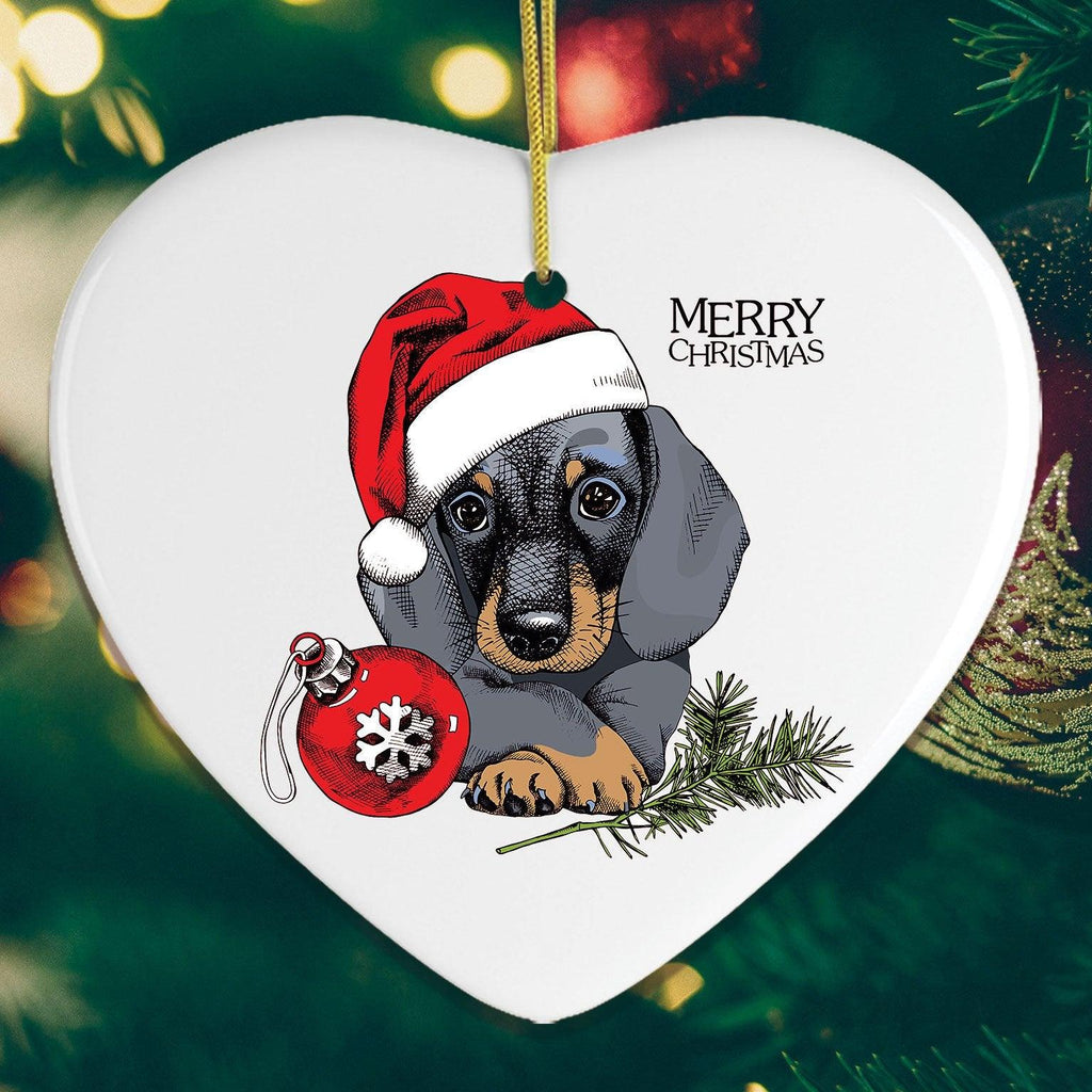 Heart-shaped Christmas ornament with a dachshund wearing a Santa hat and holding a ornament on a green background.