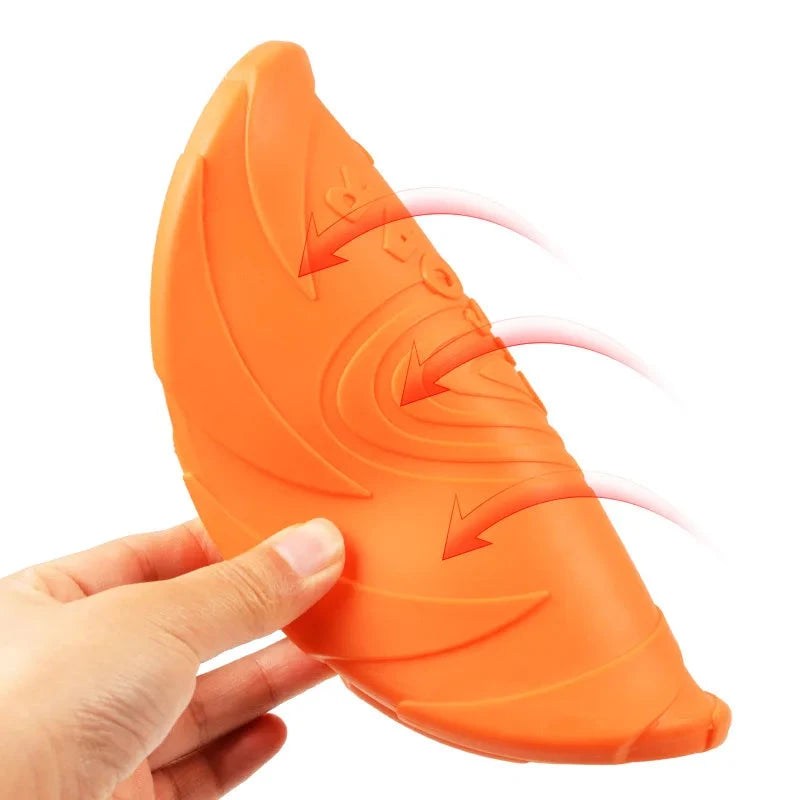 A hand is holding a Durable Silicone Dog Flying Disc – Sturdy, Bite-Resistant Outdoor Training Toy. Made from durable silicone, it features a wavy, textured surface and red arrows indicating flexibility. Ideal for outdoor training, this bite-resistant toy ensures fun and endurance. The background is plain white.