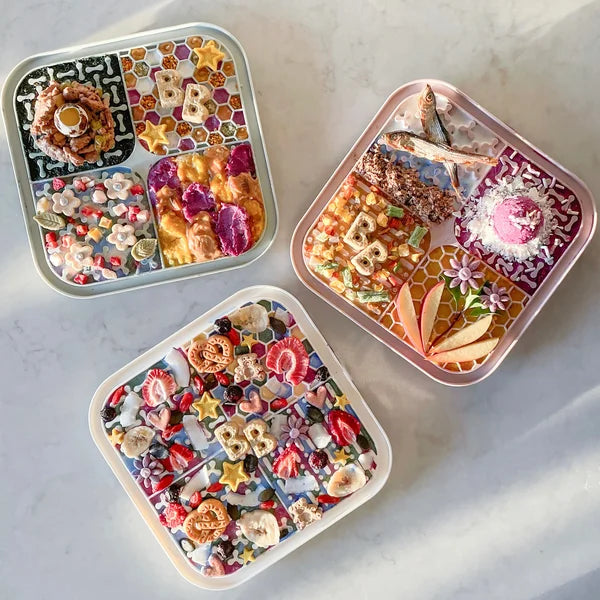 Three colorful bento boxes with various food items on a marble surface