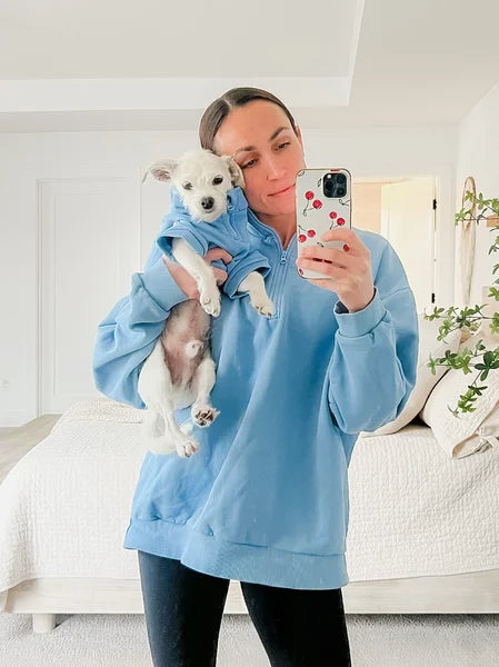 Person wearing a blue hoodie holding a small dog, taking a mirror selfie.