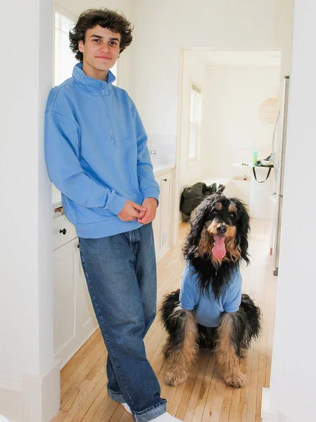 Person wearing a blue sweatshirt with a dog also wearing a blue sweatshirt in a bathroom.