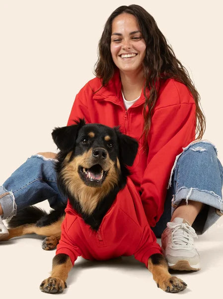 Woman in a red sweatshirt with a dog wearing a matching red outfit on a beige background