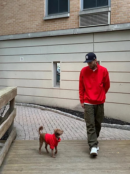 Man and dog wearing red sweaters walking on a wooden deck.