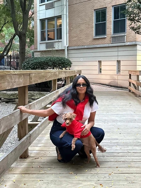 Woman in red shirt and black pants sitting on a wooden deck with a small dog.