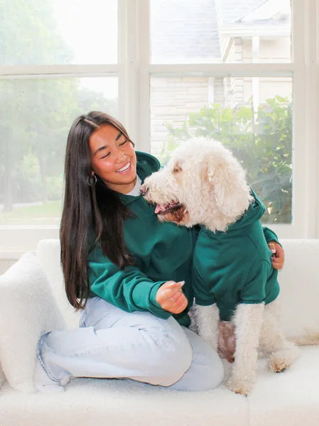 Woman in a green hoodie sitting on a couch with a white dog wearing a matching green hoodie.