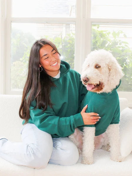 Woman in a green sweatshirt sitting on a couch with a white dog.
