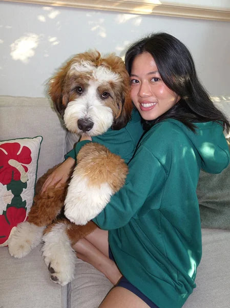 Woman in a green sweatshirt holding a brown and white dog on a couch with a floral pillow.
