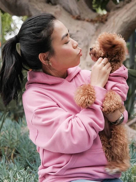 Woman in pink hoodie holding a small brown dog outdoors