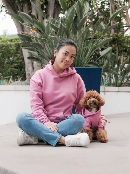 Woman in pink hoodie sitting with a dog in matching pink hoodie outdoors.