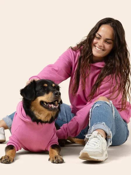 Woman in pink hoodie with a dog wearing a matching pink hoodie on a beige background