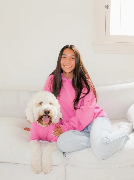 Person in a pink sweatshirt sitting on a white couch with a white dog.