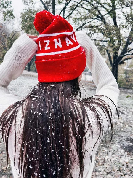 Person wearing a red beanie with 'IZNAV' branding in a snowy outdoor setting