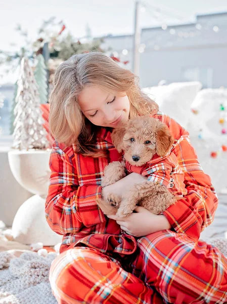 Woman in red plaid pajamas holding a small dog in a festive setting