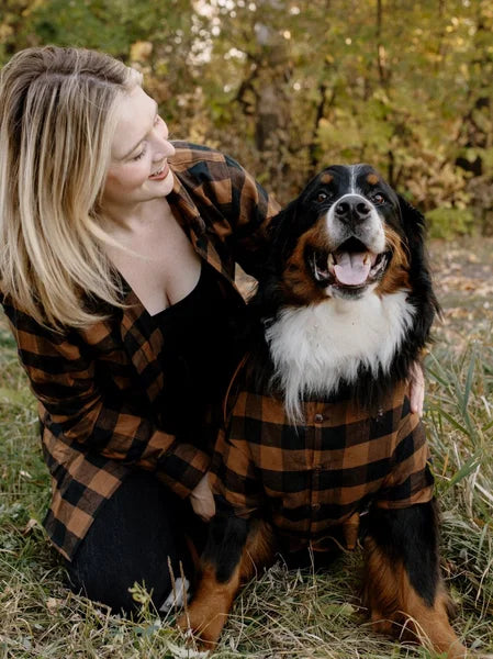 Woman and dog wearing matching plaid outfits in a natural setting