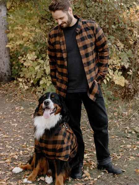 Man and dog wearing matching plaid outfits standing in a forest setting