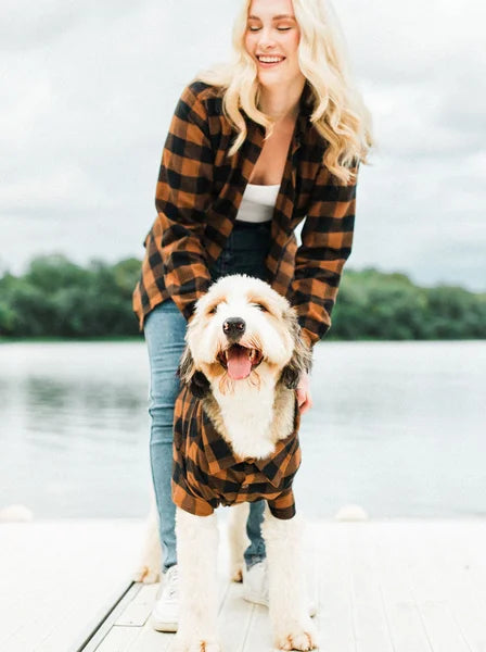Woman and dog wearing matching plaid outfits by a lake