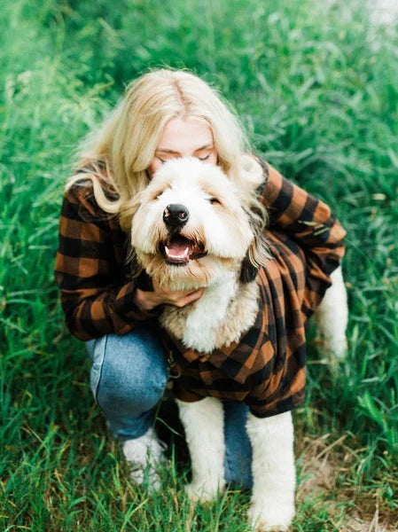 Person in plaid jacket holding a dog outdoors in grass
