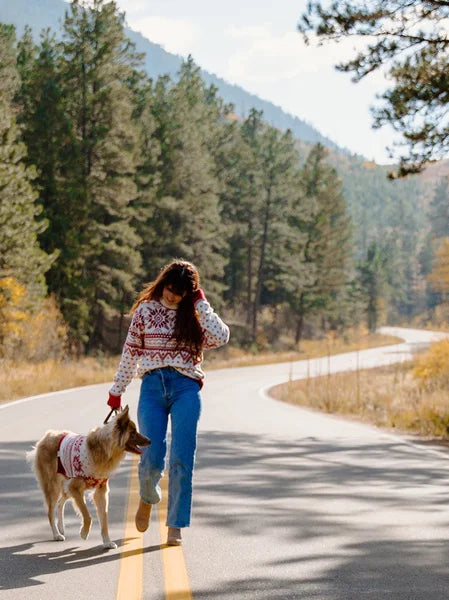 Woman walking a dog on a road surrounded by trees and mountains
