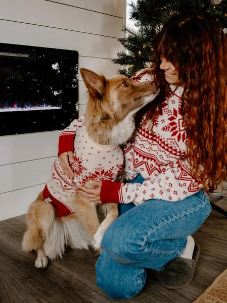 Woman and dog wearing matching red and white sweaters in front of a Christmas tree.