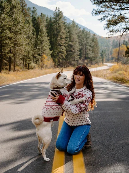 Woman and dog on a road trip, with the woman holding a dog in a sweater.