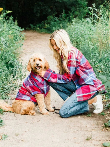 Woman and dog wearing matching plaid outfits outdoors on a path.