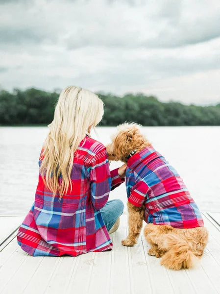 Woman and dog wearing matching plaid shirts sitting on a dock.