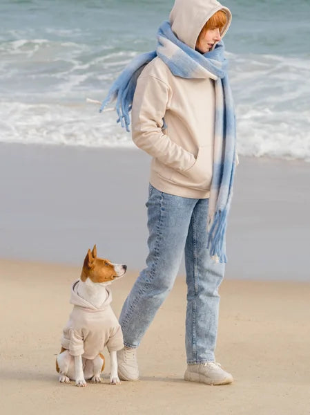 Person and dog on a beach wearing matching outfits with a blue scarf.