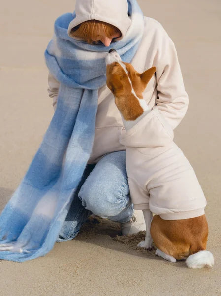 Person in a white outfit with a blue scarf and a dog on a sandy surface