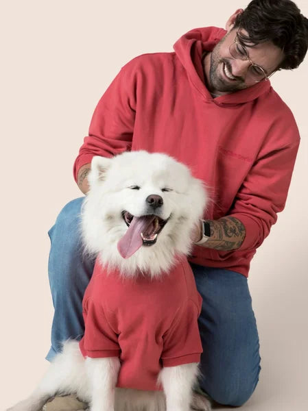 Man in a red hoodie with a white dog wearing a matching red sweater on a beige background