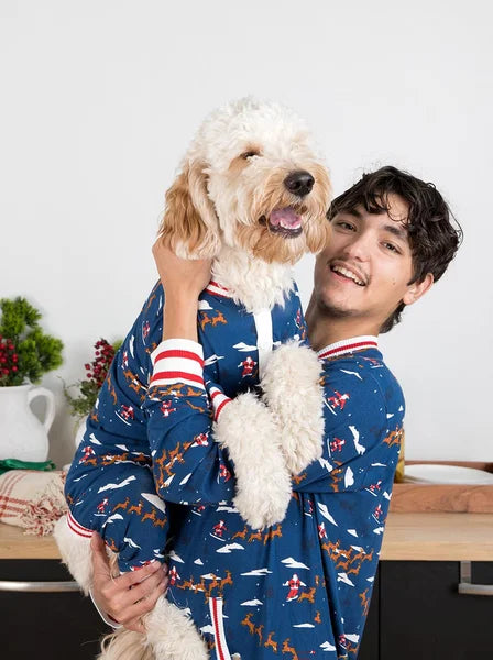 Person wearing a blue pajama with animal patterns holding a white dog.