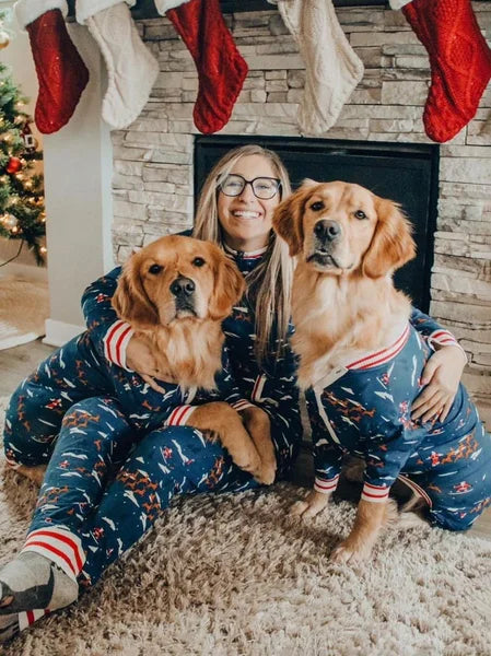 Woman and two dogs in matching pajamas sitting in front of a fireplace with Christmas stockings.