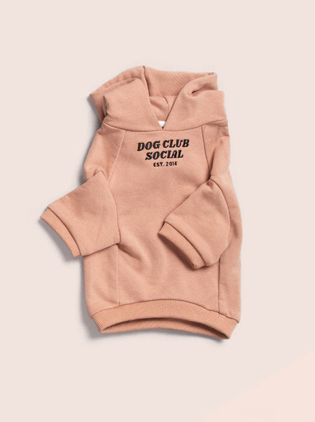 Pink dog hoodie with 'Dog Club Social' text on a beige background