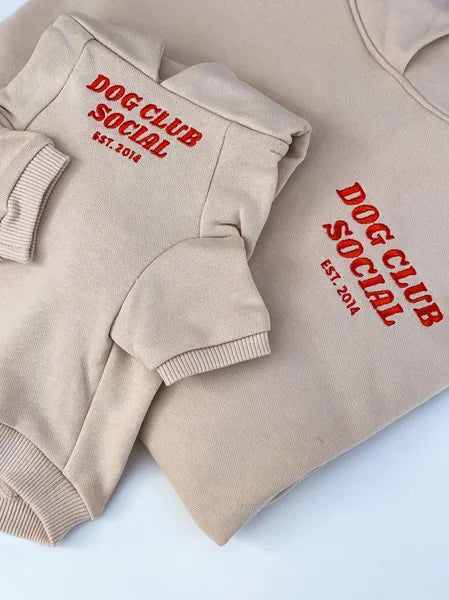 Beige hoodie with red 'Dog Club Social' text on a light blue background