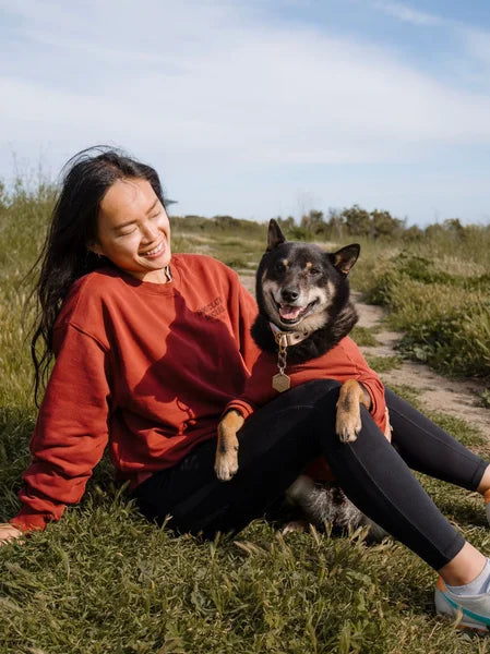 Woman in a red sweatshirt sitting on grass with a dog