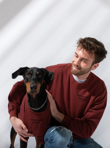 Man and dog wearing matching red sweatshirts against a white background