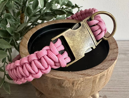 Pink paracord keychain with a metal clip on a wooden surface with plants in the background