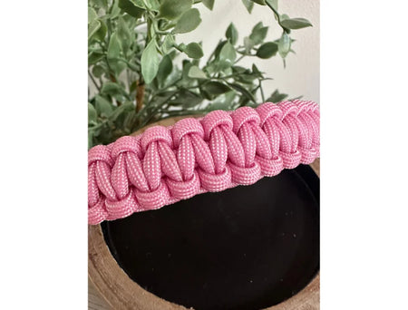Pink braided band on a black pot with green plants in the background