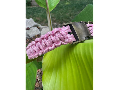 Pink paracord bracelet with metal clasp on a green leaf