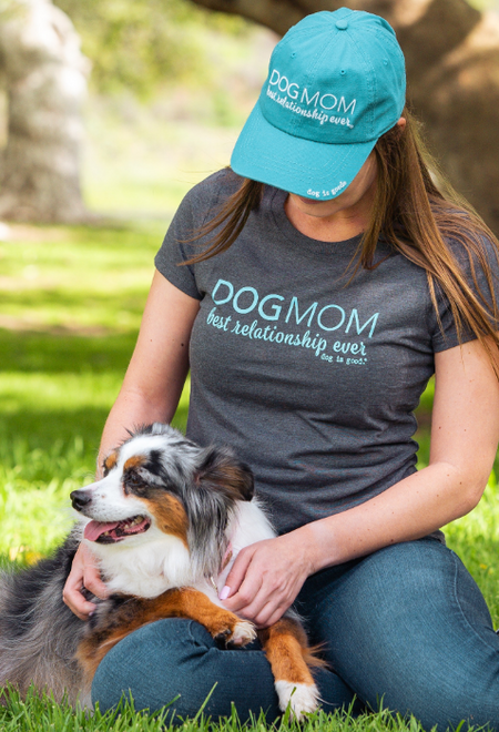 Person wearing a 'Dog Mom best relationship ever' shirt and cap, sitting with a dog outdoors.