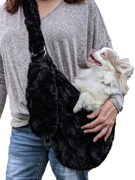 Person holding a dog in a black fluffy pet sling against a white background