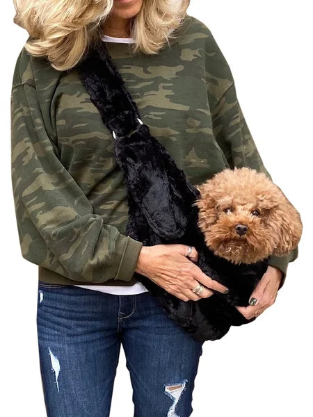 Person wearing a camouflage sweatshirt with a black pet carrier holding a small brown dog.