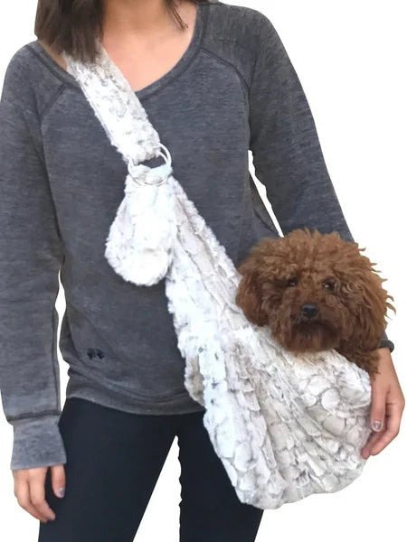Person holding a white lace dog sling with a brown dog inside, wearing a gray long-sleeve shirt.