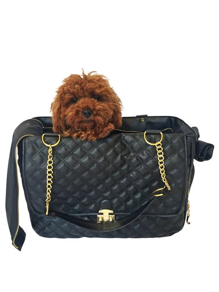 Dog peeking out from a black quilted handbag with gold accents on a white background