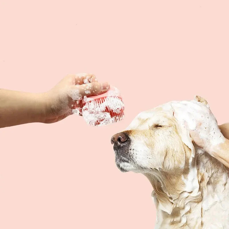 A person's hand covered in soap lathers a **Soft Silicone Bath Massage Brush for Dogs - Gentle, Effective Grooming & Relaxation** on the head of a golden retriever, who has its eyes closed and looks relaxed. The dog's wet and soapy fur shows it's enjoying this comfortable and safe dog grooming session against a solid peach background.