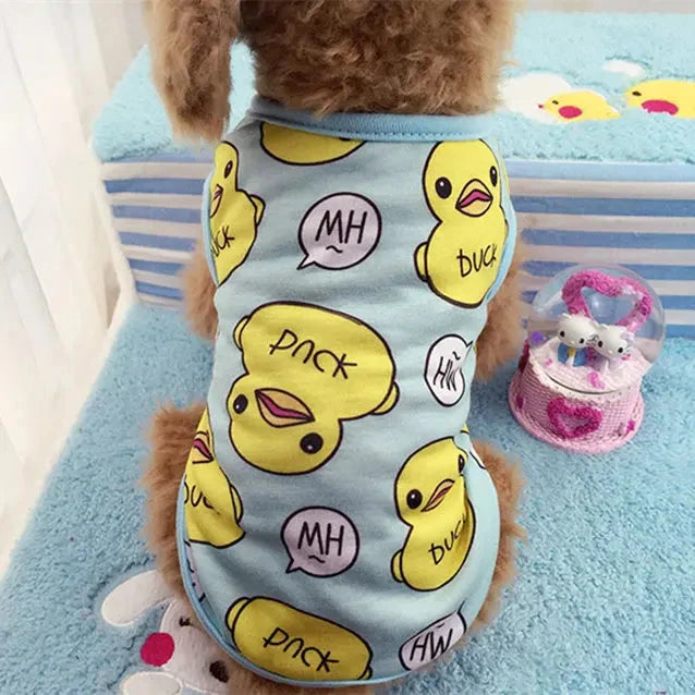 A small dog is wearing Adorable Spring & Summer Puppy Pajamas - Soft, Stylish Dog Outfits for Small Breeds, specifically a light blue shirt adorned with cartoon yellow ducklings and speech bubbles saying 