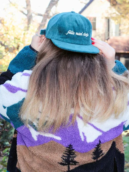 Person wearing a teal cap with text and a patterned sweater outdoors